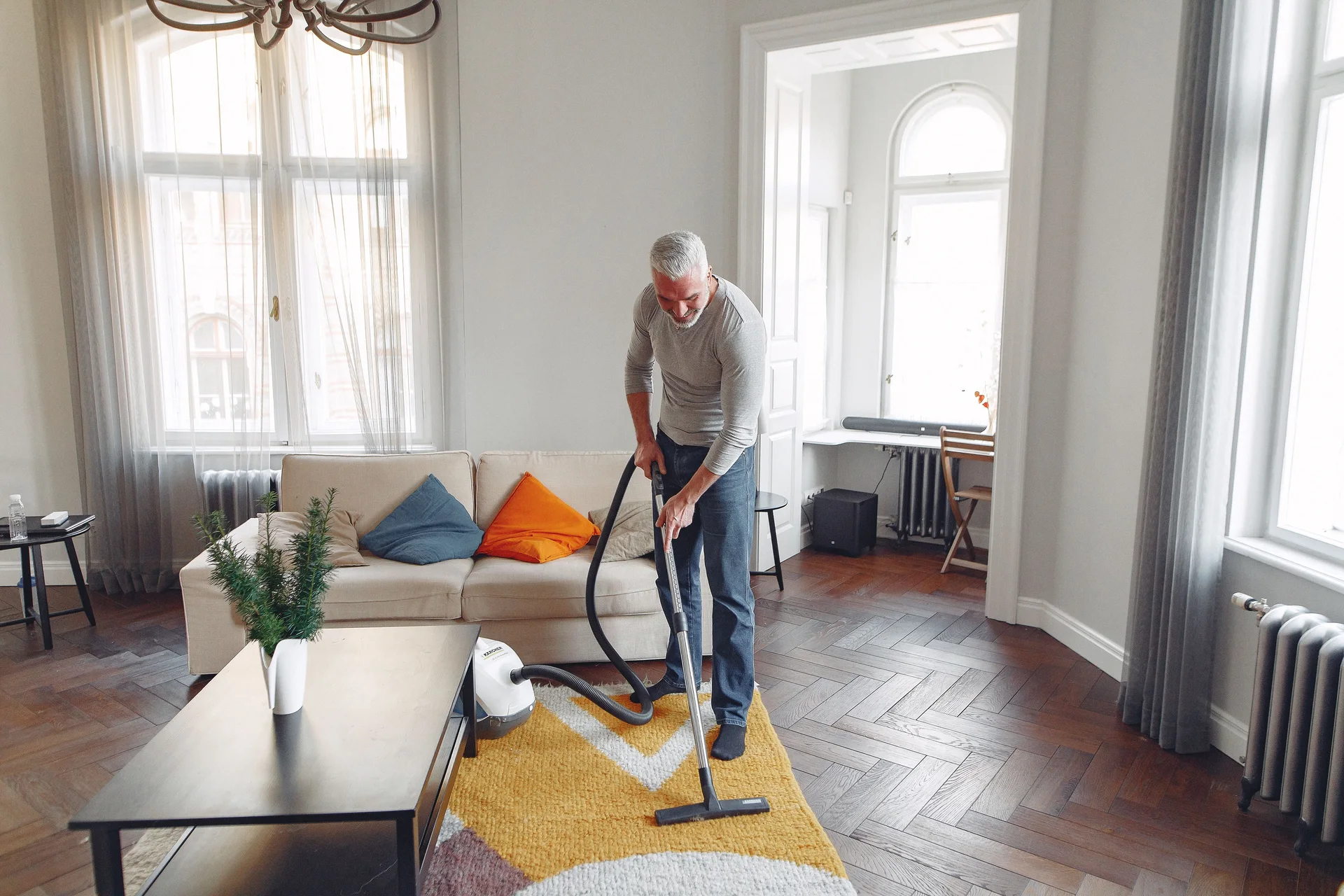 A homeowner using a portable canister vacuum in a bright, tidy living room